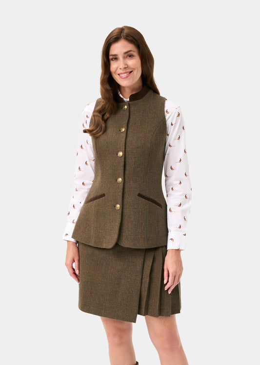 A woman modeling a brown tweed vest and matching pleated skirt set, worn over a white long-sleeve shirt with a small paisley print, against a light gray studio background.
