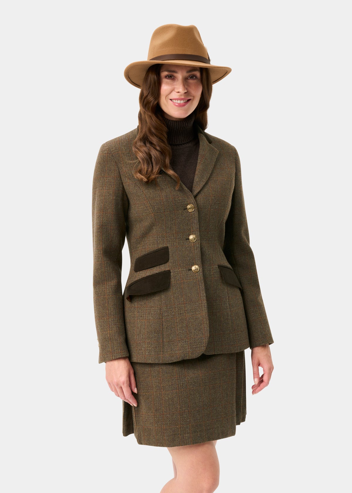 A woman wears a Surrey Ladies Tweed Water Repellent Blazer in Field Maple and matching skirt with a tan hat and turtleneck.