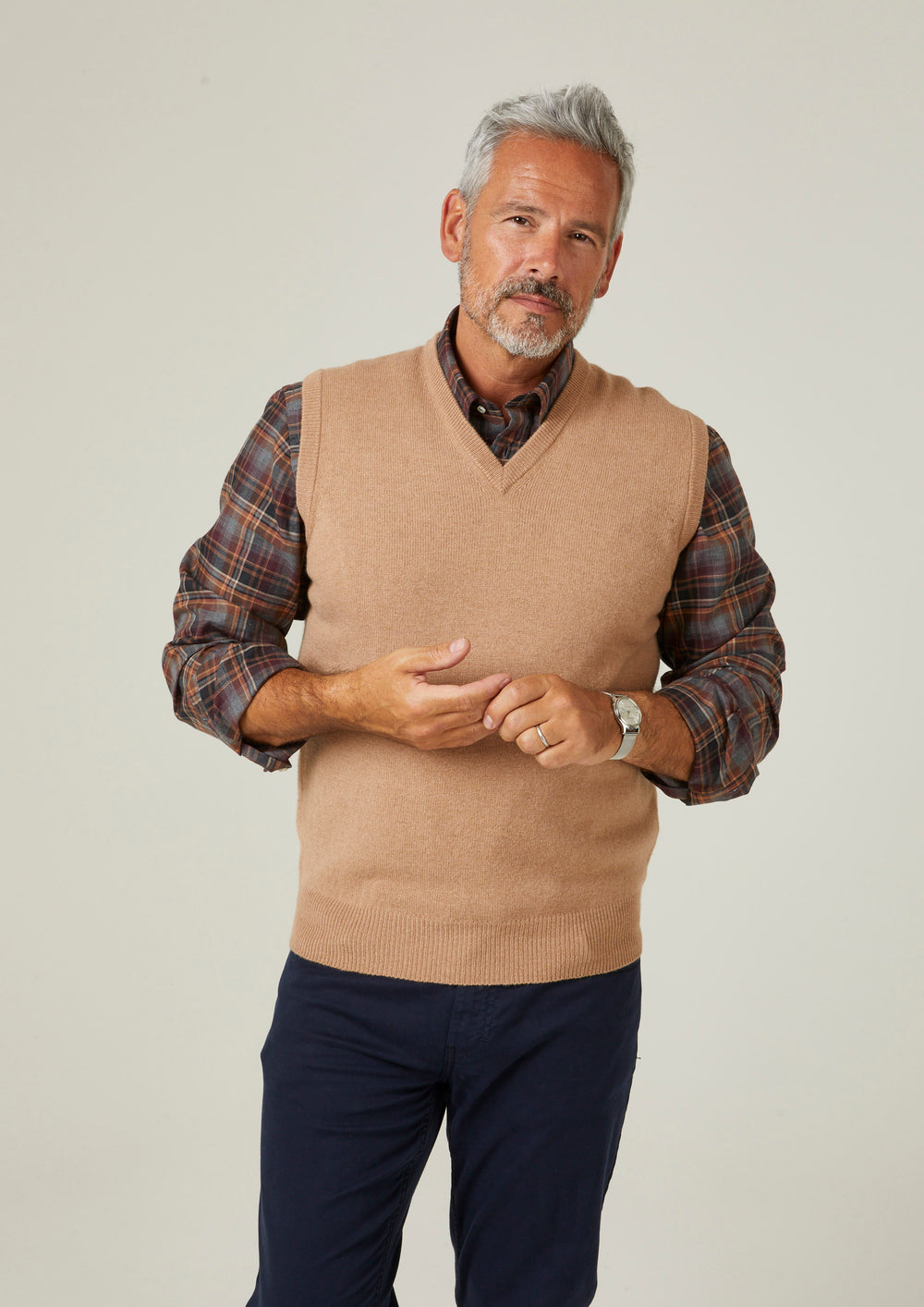 A man wearing a camel Norfolk Lambswool V-Neck Slipover In Classic Fit over a plaid shirt and dark trousers.